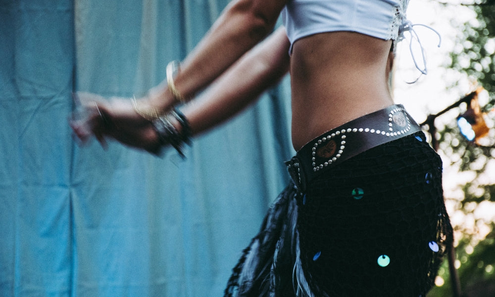 Close-up of a woman in a white cropped baby tee and low-rise studded skirt dancing outdoors