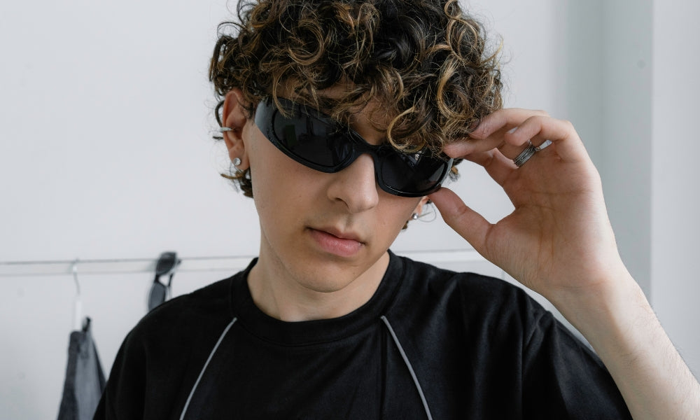 Person wearing black wraparound shield sunglasses and a black technical t-shirt with contrast piping