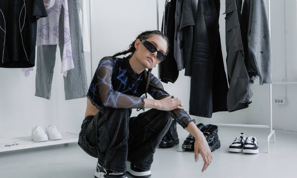 Woman in sheer top and black low-rise cargo jeans crouching in a clothing store surrounded by denim and streetwear