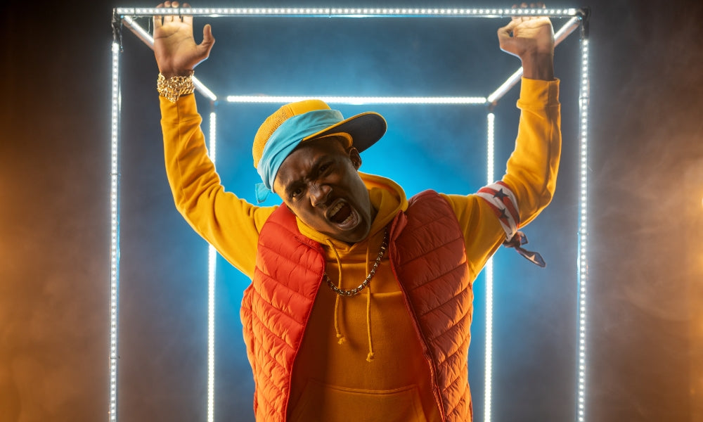 Man in colorful mesh trucker cap and orange puffer vest shouting with raised arms in front of illuminated cube frame